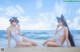 Two women in white bathing suits sitting on the beach.