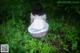 A woman in a white dress is sitting in the grass.